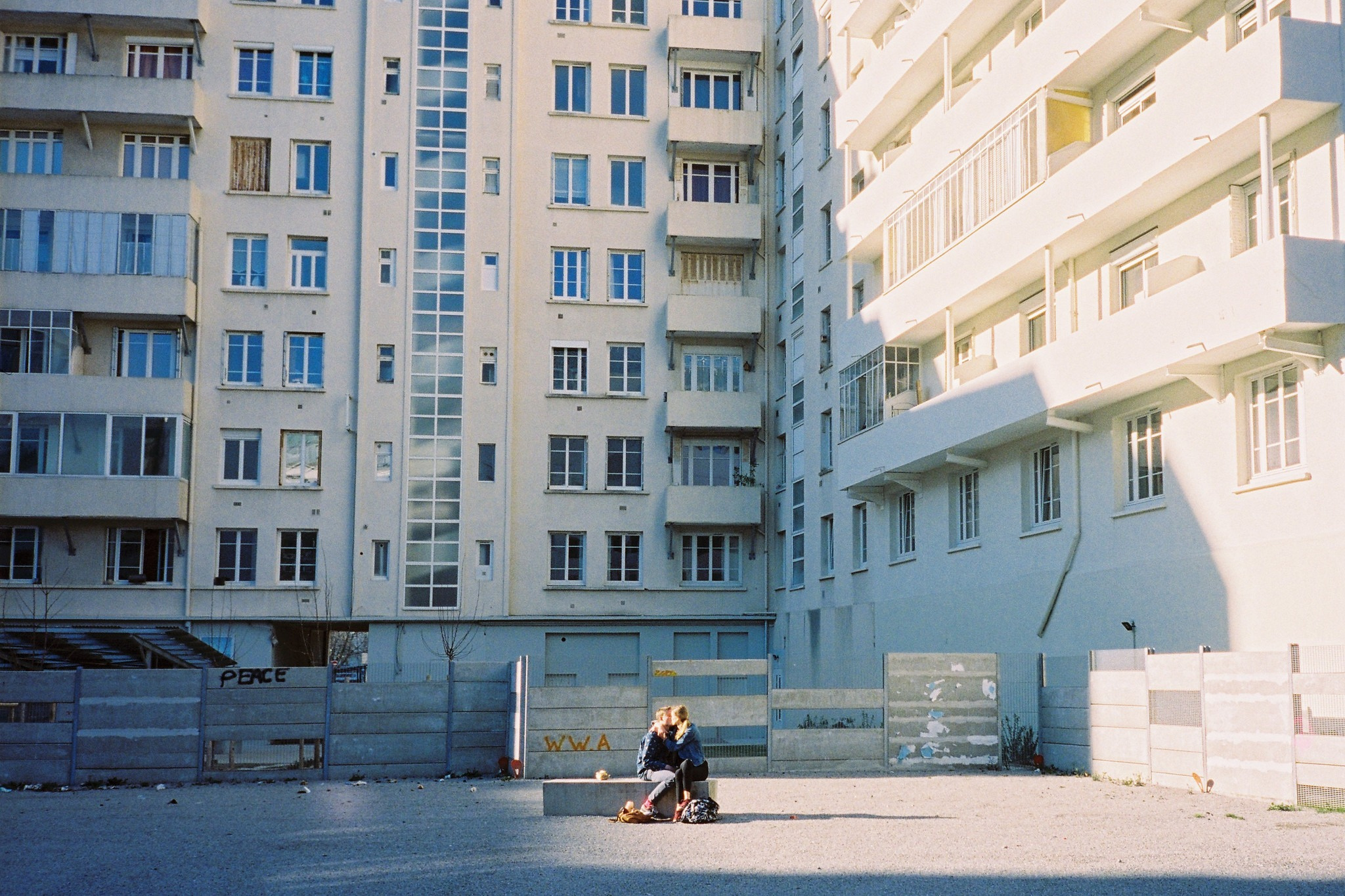 Two people sharing a moment on a bench in a sunlit apartment courtyard