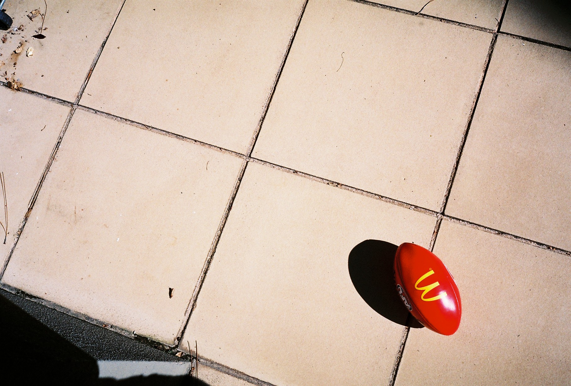 A red football casting a hard shadow on sun-bleached paving