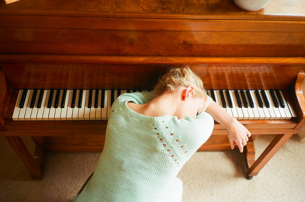 A woman in a mint jumper resting her head on the keys of a timber piano