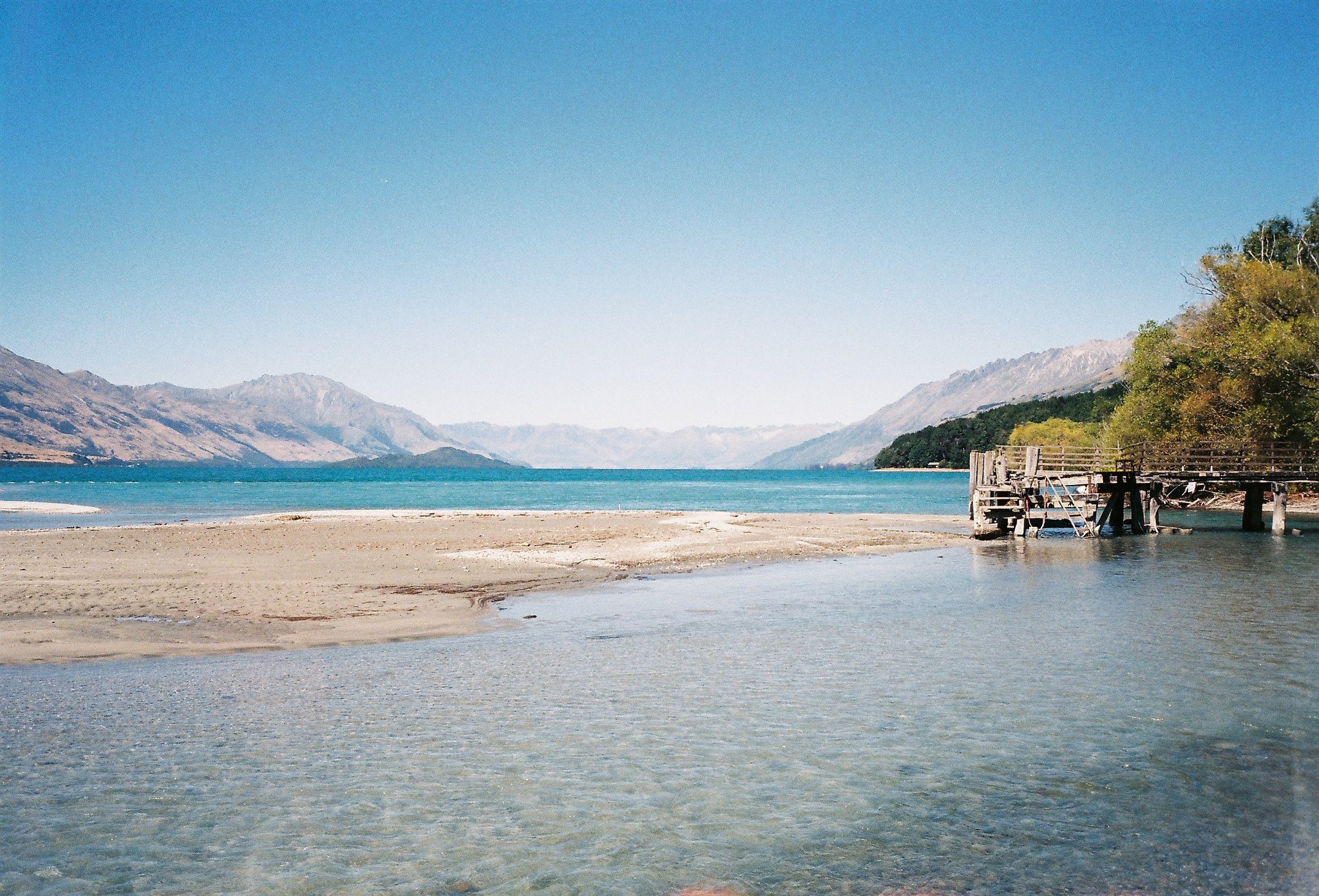 A clear alpine lake with a wooden jetty and mountains under a blue sky