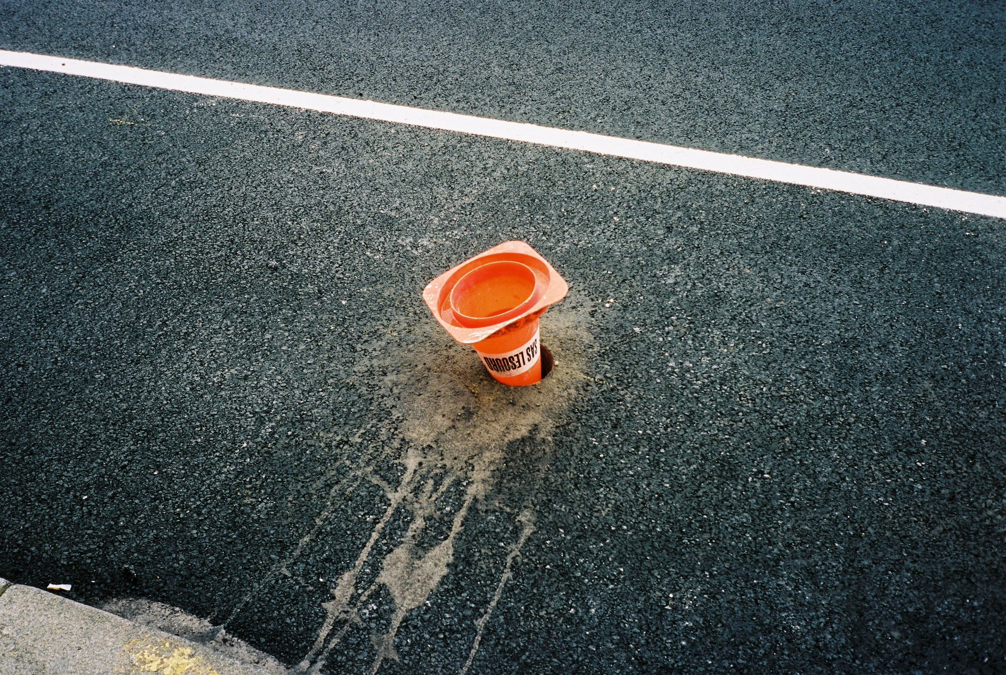 A crushed orange traffic cone sunk into fresh asphalt